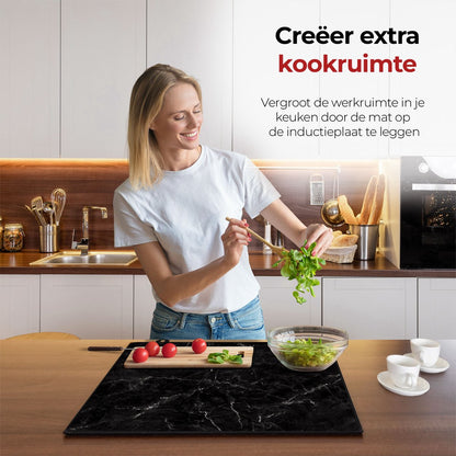 Mujer en la cocina preparando comida con la ayuda del protector de inducción mármol negro y blanco.