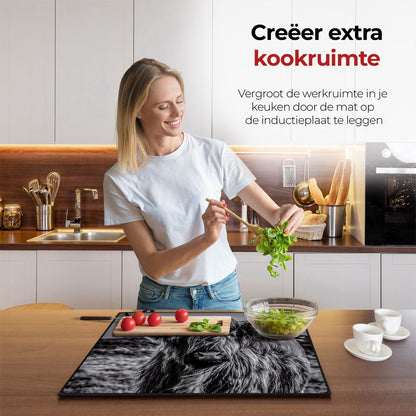 Mujer en la cocina preparando comida con la ayuda del protector de inducción Highlander escocés blanco y negro.